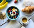 top view of strawberry and berries parfait in bowl near croissant and laptop