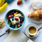 top view of strawberry and berries parfait in bowl near croissant and laptop