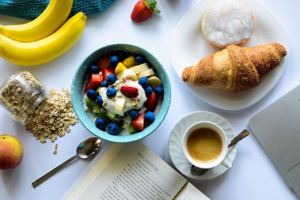 top view of strawberry and berries parfait in bowl near croissant and laptop