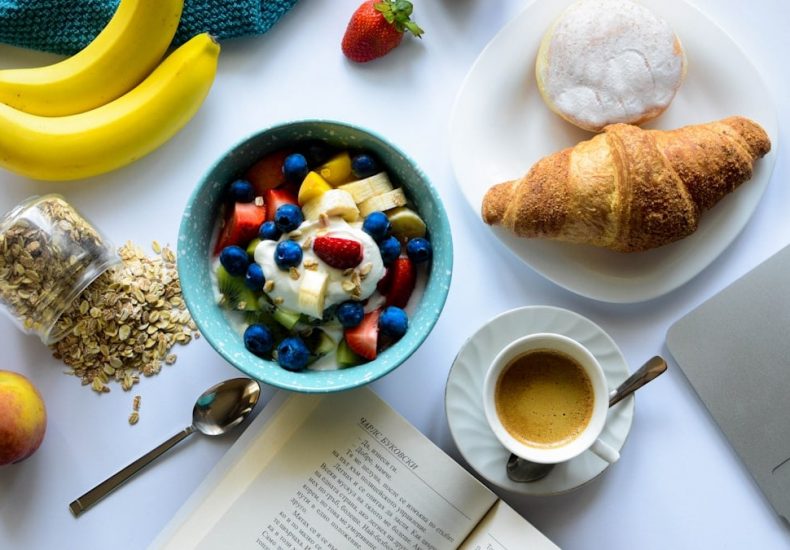 top view of strawberry and berries parfait in bowl near croissant and laptop