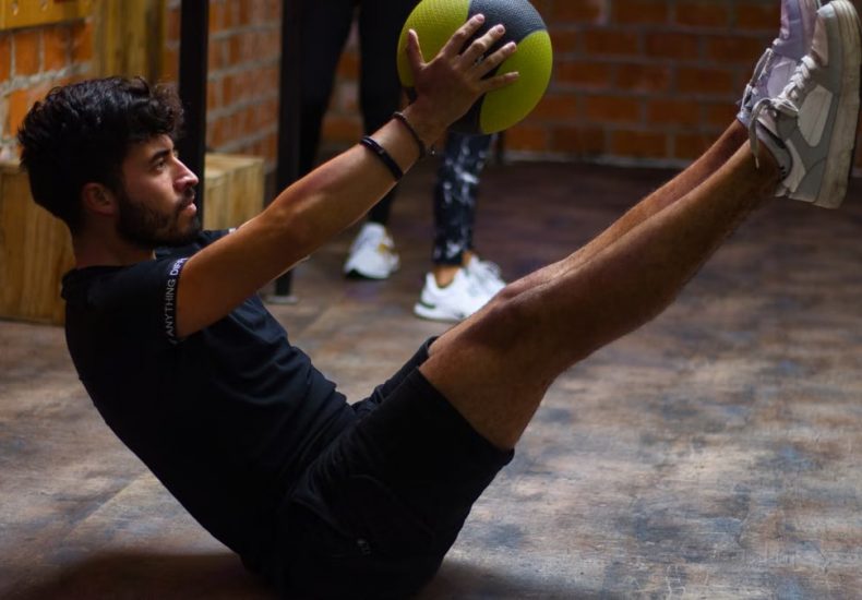 Focused man performing core exercises with a medicine ball in an indoor gym highlighting fitness and strength.